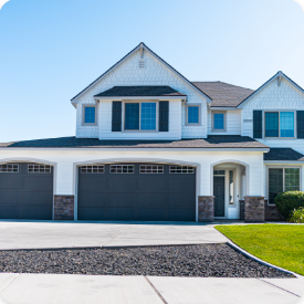 A modern, two-story house with white siding and dark gray accents. The exterior boasts a three-car garage with dark gray doors, a tidy green lawn, and a paved driveway. With clear blue skies above, it's an ideal scene for the charm of residential or commercial painting services.