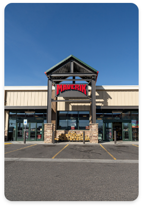 A store with a red "Maverik" sign above the entrance has a modern rustic design, featuring stone pillars and a wooden awning. The front area, enhanced by commercial painting services, boasts neatly stacked firewood, large glass windows, and an adjacent parking space.